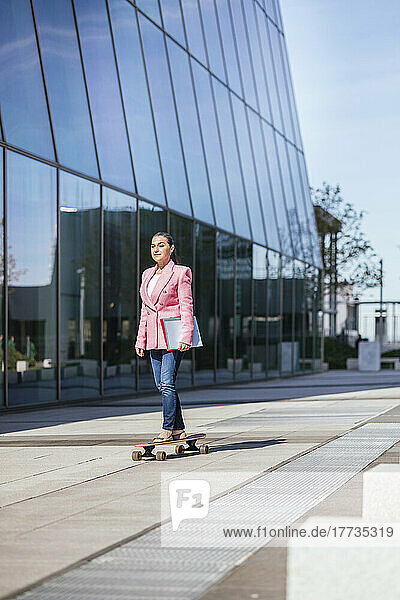 Mature businesswoman skateboarding by modern office building