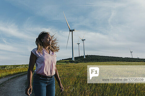 Lächelnde Frau mit zerzausten Haaren steht vor einer Windkraftanlage