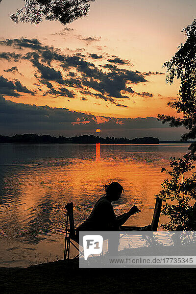 Silhouette einer Frau malt am See bei Sonnenuntergang