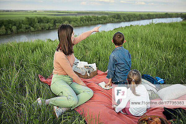 Young woman by children pointing at river by field