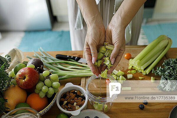 Hands of woman putting chopped celery in juicer at home