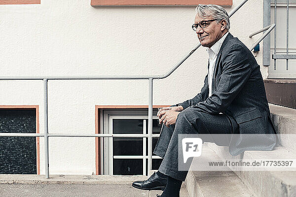 Contemplative senior businessman sitting on steps outside building