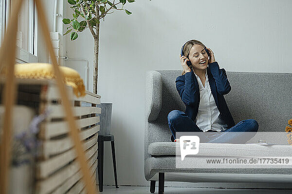 Happy businesswoman enjoying music listening through wireless headphones on sofa in office