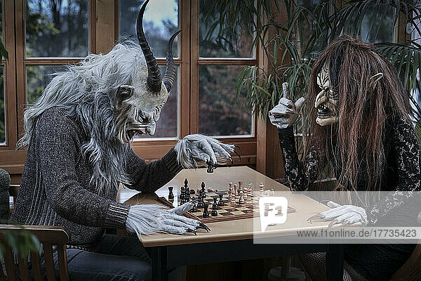Reifer Mann und Frau im Geisterkostüm spielen Schachspiel am Tisch sitzend