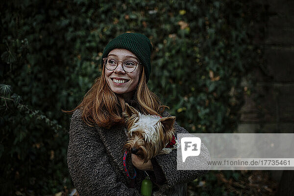 Happy woman wearing knit hat with Yorkshire Terrier at park