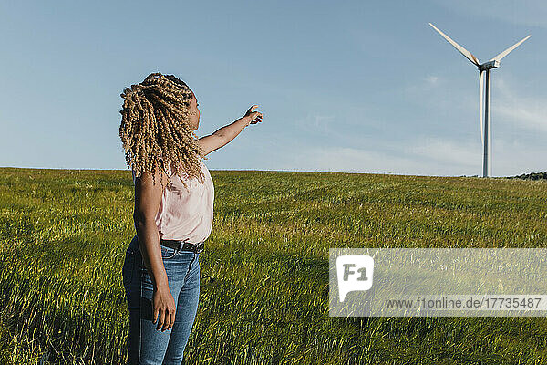 Junge Frau zeigt auf eine Windmühle  die auf einer Wiese steht