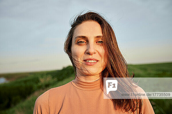 Smiling young woman with brown hair in field at sunset