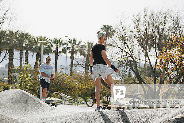 Lächelnde Frau mit Skateboard vor Freund auf Sportrampe