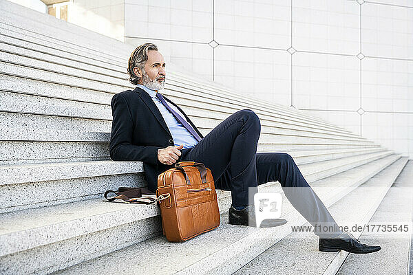 Thoughtful businessman sitting by bag on steps