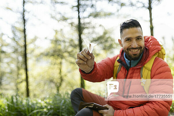 Smiling hiker with paper airplane sitting in forest