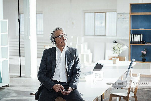 Senior businessman with eyes closed enjoying music listening through headphones in office