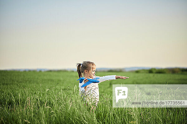 Nettes Mädchen  das bei Sonnenuntergang mit Flugzeugspielzeug auf dem Feld spielt