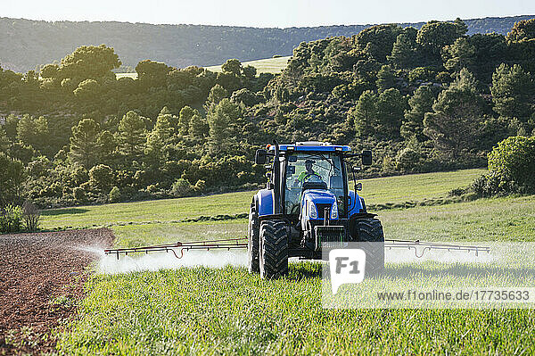 Young farmer sitting in tractor spraying fertilizer on field