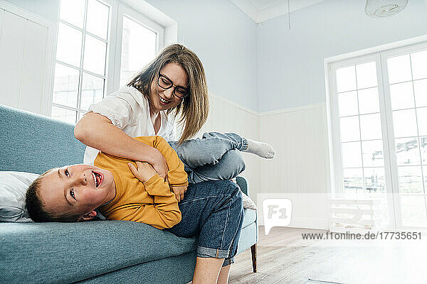 Happy mother playing with son on sofa at home