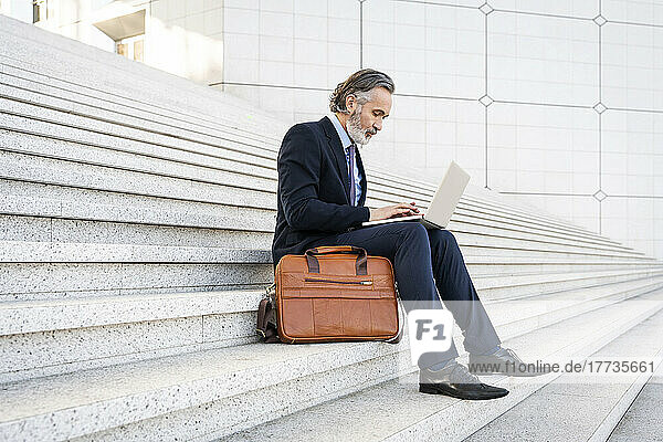 Mature businessman using laptop sitting on steps