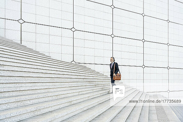 Mature businessman with bag moving up on steps