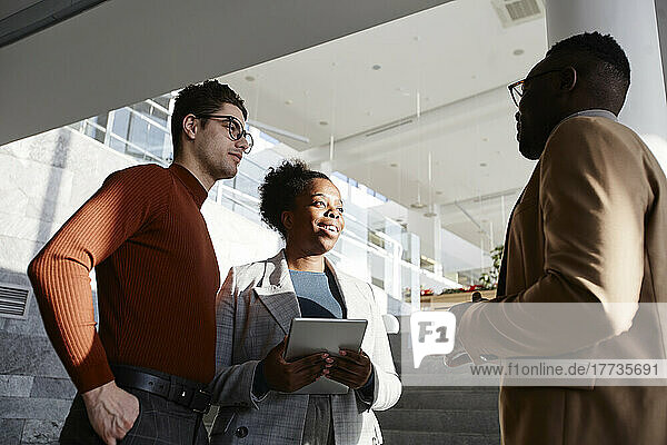 Young businessman and businesswoman looking at colleague discussing in office