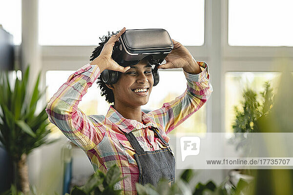 Happy gardener holding virtual reality headset at plant nursery