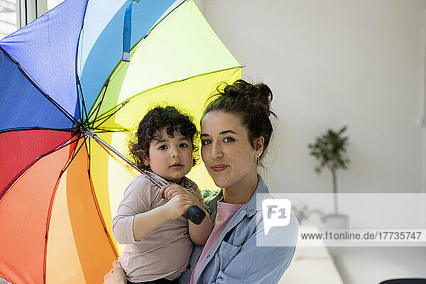 Mother and daughter standing at home holding umbrella