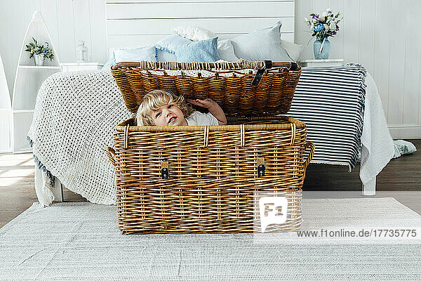 Cute boy sitting in wicker basket at home