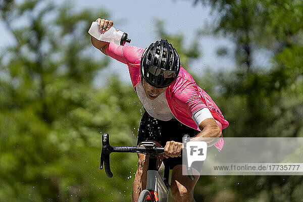 Sportler  der an einem sonnigen Tag Fahrrad fährt und Wasser aus der Flasche gießt