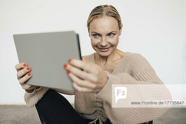 Smiling woman holding tablet PC in front of wall