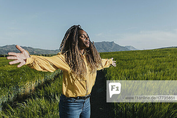 Young woman standing with arms outstretched in meadow on sunny day
