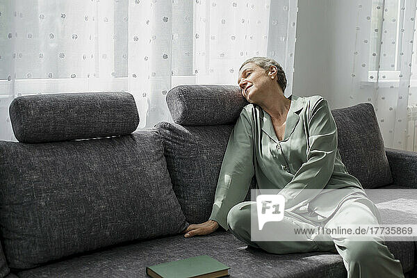 Relaxed mature woman sitting on couch in living room with closed eyes