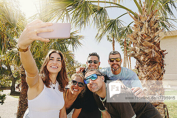 Smiling young woman with friends taking selfie through smart phone