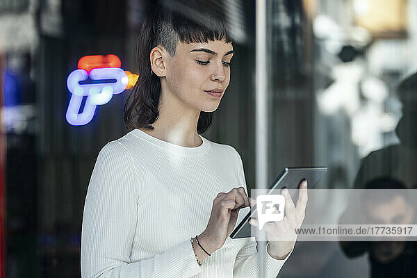 Woman in restaurant using tablet PC seen through glass door