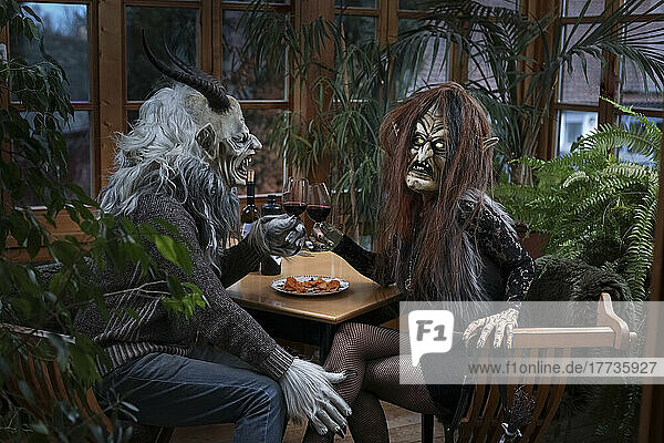 Mann und Frau in gruseligem Kostüm stoßen am Tisch mit Weingläsern an