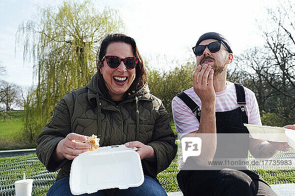 Happy woman having burger with friend in park