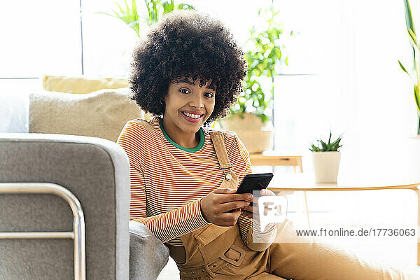 Smiling woman holding mobile phone leaning on sofa at home
