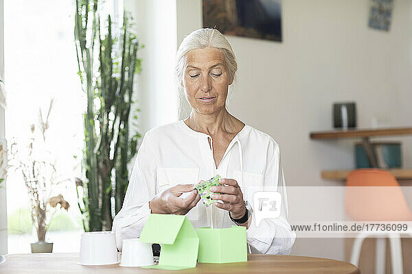 Mature woman making house model from recycled material at home