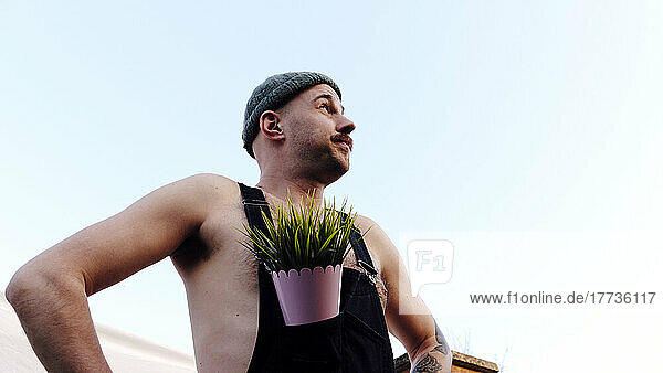Man wearing knit hat standing with plant in bib overalls