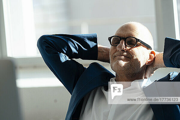 Senior businessman sitting with hands behind head relaxing in office