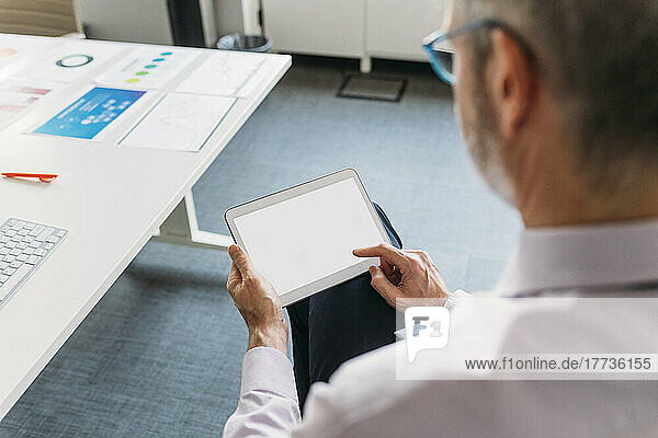 Businessman using tablet PC sitting by desk in office