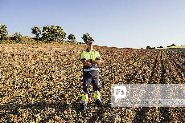 Farmer with arms crossed standing on field on sunny day