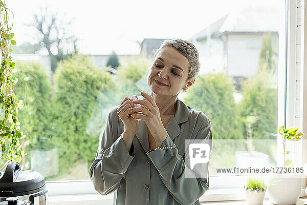 Mature woman holding tea glass at the window at home