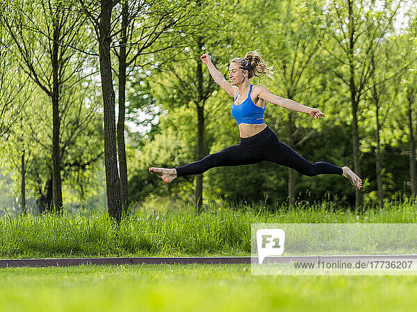 Smiling woman jumping with arms outstretched over meadow at park