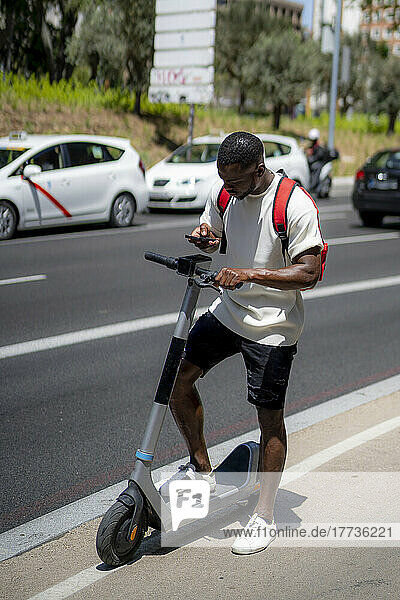 Young man with electric push scooter using smart phone on road