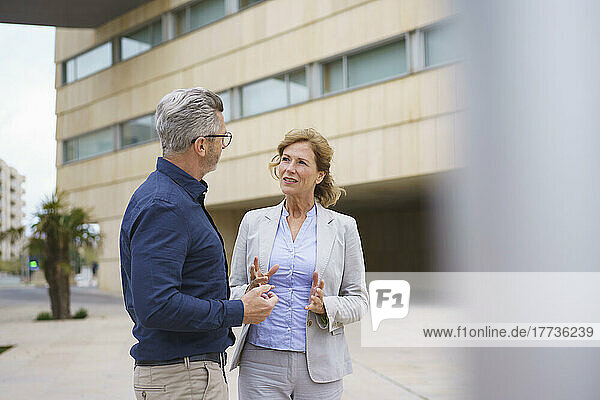 Geschäftsfrau diskutiert mit Geschäftsmann vor Bürogebäude