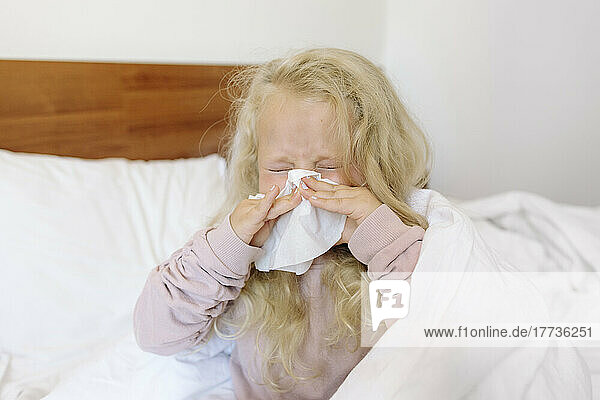 Blondes Mädchen putzt sich im Schlafzimmer mit Seidenpapier die Nase