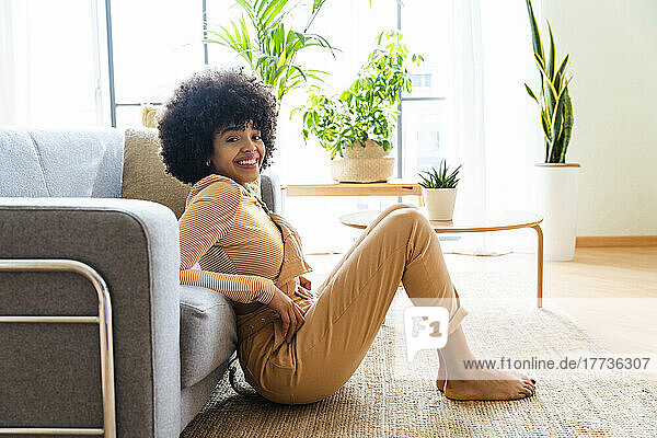 Smiling Afro woman leaning on sofa at home