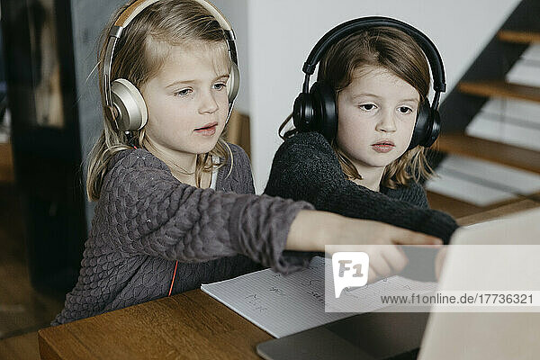 Sisters with headphones pointing at laptop doing E-learning at home