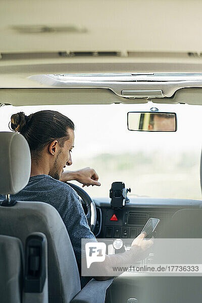 Junger Mann  der im Transporter sitzt und Textnachrichten über sein Smartphone sendet