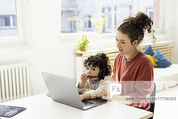Little girl with headset sitting on lap of mother using laptop