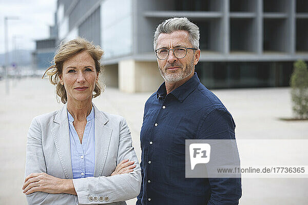 Businesswoman with arms crossed standing by businessman wearing eyeglasses