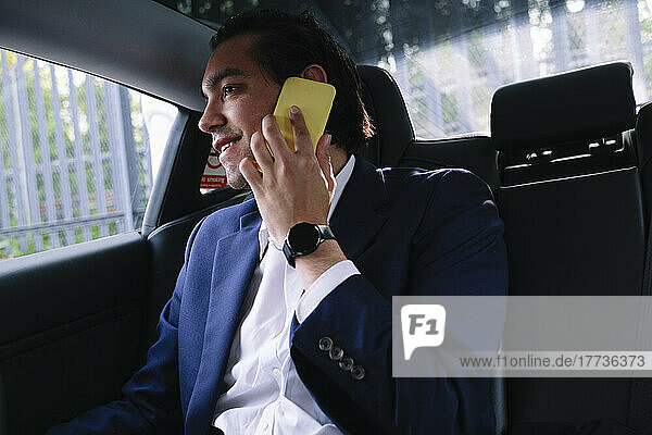 Smiling businessman talking on smart phone sitting in electric car