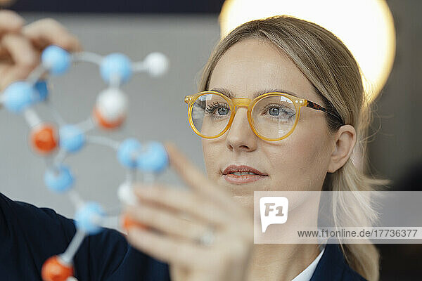 Businesswoman wearing eyeglasses examining molecular model in office